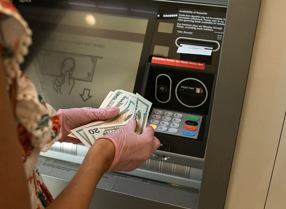 mulher contando dinheiro na frente de um caixa eletrônico